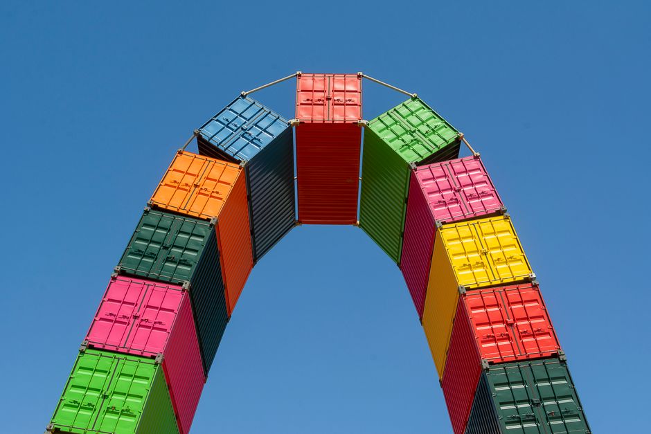 A vibrant display of stacked shipping containers forming an arch under a clear blue sky.