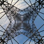 Looking up through a steel power tower against a blue sky and clouds.
