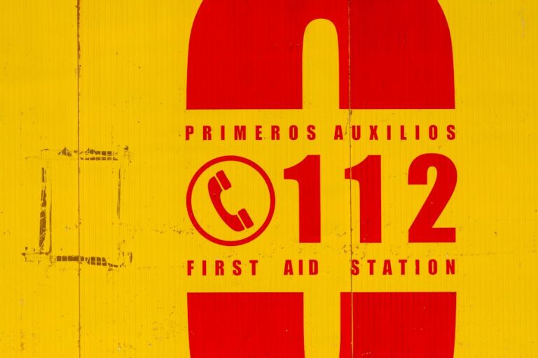 Bright yellow and red emergency sign indicating first aid station. Call 112 for emergencies.
