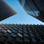 Low angle view of modern skyscrapers with glass panels reflecting under a blue sky.