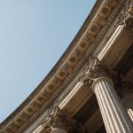 The Architecture of Legitimacy: Lessons in Leadership from 1060 Detailed low-angle view of classical columns against a clear sky reflecting historical architectural grandeur.