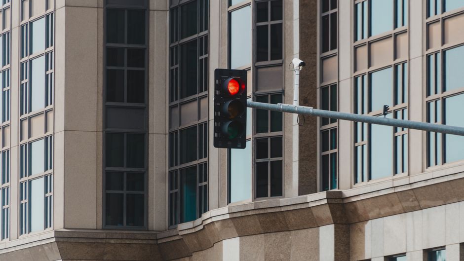 Red traffic light in cityscape setting with modern glass building facade.