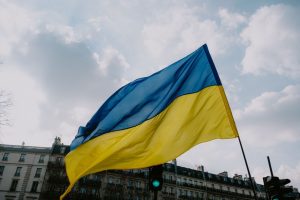 Waving Ukrainian flag against a cloudy sky and city skyline, symbolizing national pride.