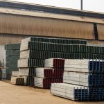 Outdoor view of an industrial warehouse with multiple stacks of metal beams and pallets.
