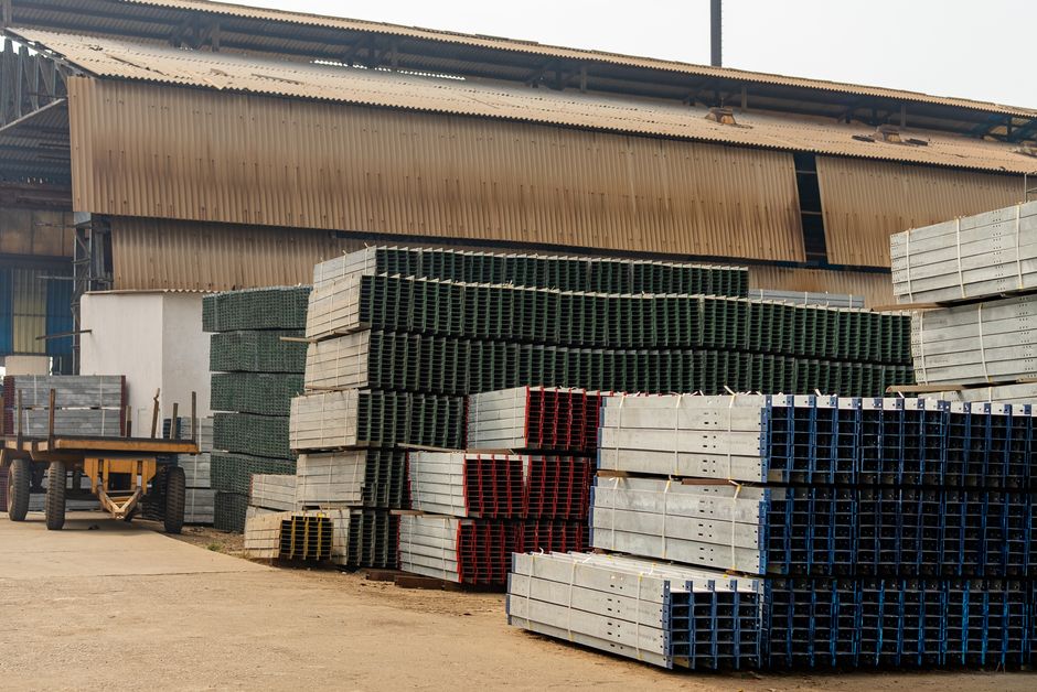 Outdoor view of an industrial warehouse with multiple stacks of metal beams and pallets.