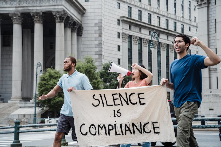 Activists marching with a banner saying 'Silence is Compliance' outside a courthouse.