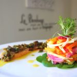 A vibrant stack of fresh vegetables artfully plated, served with a gourmet dressing.