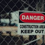 The Danger of Over-Connection: Why Strategic Isolation is the High-Performer’s Secret Weapon Close-up of a warning sign on a chain link fence at a construction site indicating danger.