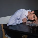 The Dopamine Debt: Why High-Performers Must Audit Their 'Success' Addiction Man resting head on a desk covered with bills, looking stressed and overwhelmed.