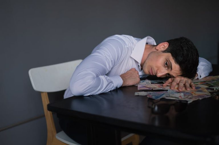 Man resting head on a desk covered with bills, looking stressed and overwhelmed.