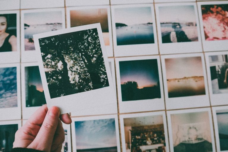 A close-up of a hand holding a Polaroid picture among a collection of vintage photographs indoors.