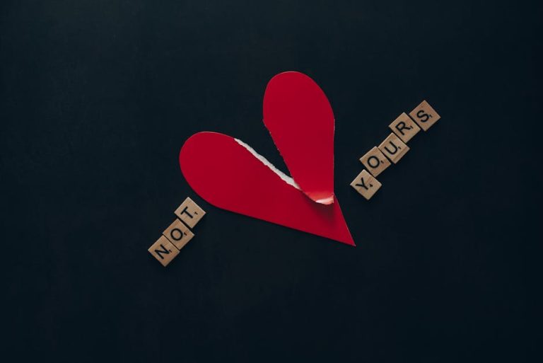 Conceptual image of a torn red heart with Scrabble tiles spelling 'NOT YOURS' on a dark background.