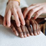 Close-up of hands reading a braille book together, emphasizing support and learning.
