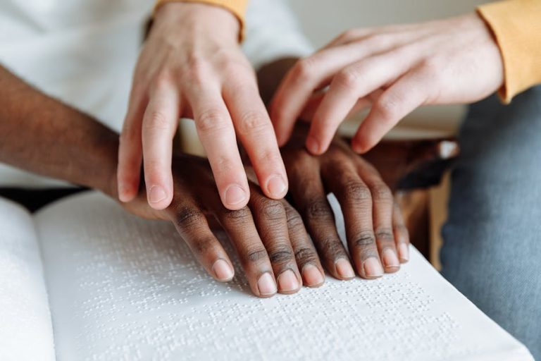 Close-up of hands reading a braille book together, emphasizing support and learning.