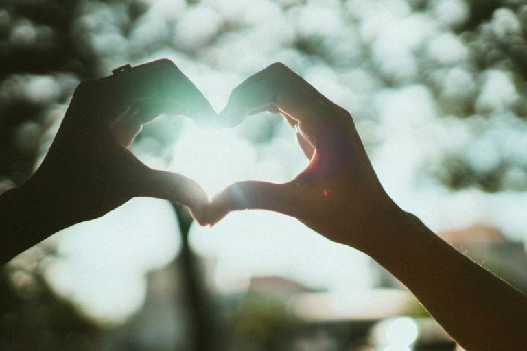 Close-up of hands creating a heart shape under bright sunlight, symbolizing love and connection.