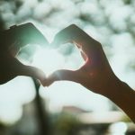 The Empathy Trap: Why Over-Optimizing Human Connection is Killing Your Output Close-up of hands creating a heart shape under bright sunlight, symbolizing love and connection.