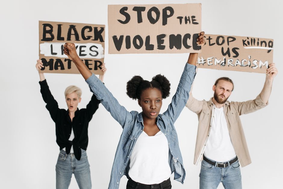 Three adults holding protest signs advocating against racism and violence on a white background.