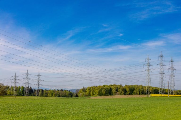 High voltage power lines stretch across a lush green field in Winterthur, Switzerland.