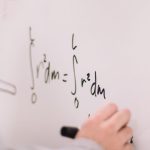 The Engineering of Moral Calculus in Autonomous Robotics Person writing math equations on a whiteboard, focusing on integrals and formulas.