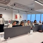 Team of professionals working in a modern office setting with computers and open workspace.