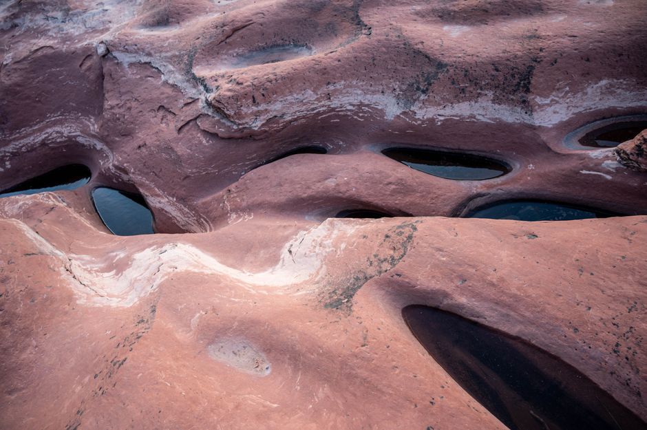 Aerial view of red sandstone formations with unique eroded patterns and water pools.
