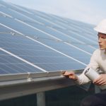Focused young male employer in formal wear and hardhat working on solar panel station and checking details of modules