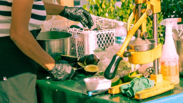 Street vendor in gloves preparing fresh avocado using citrus press outdoors.