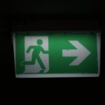 The Exit Strategy Paradox: Why Great Leaders Must Engineer Their Own Irrelevance Illuminated green emergency exit sign with an arrow pointing right in a dark setting.
