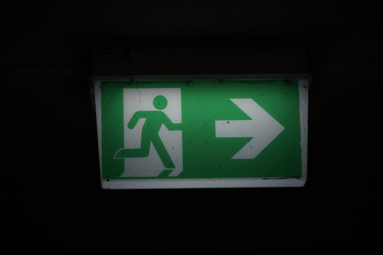 Illuminated green emergency exit sign with an arrow pointing right in a dark setting.