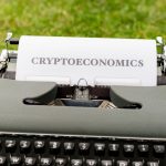 An antique typewriter with cryptoeconomics text on paper against a grassy background.