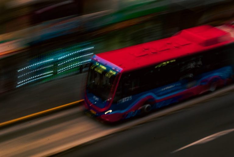Motion blur shot of a red bus speeding through a city street at night.