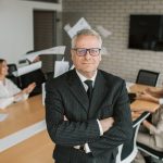 The Fiction Fallacy: Why Leaders Should Abandon 'Business Books' for Narrative Complexity Business executive standing confidently in meeting room with team engaged in discussion behind.