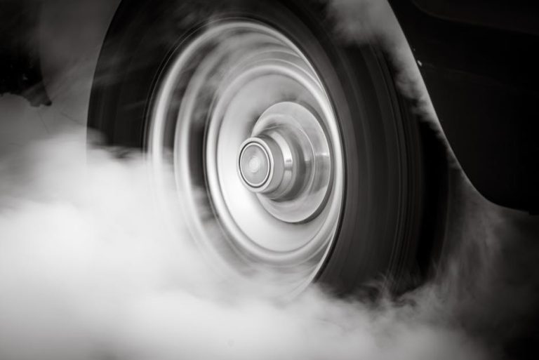 Dramatic black and white image of a spinning car wheel producing smoke, depicting speed and motion.
