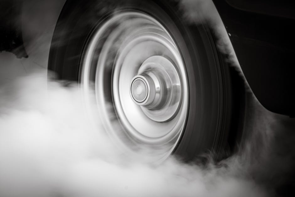 Dramatic black and white image of a spinning car wheel producing smoke, depicting speed and motion.