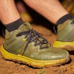 Close-up of green hiking shoes on a muddy path, emphasizing adventure and outdoor activity.
