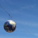The Future of Inter-planetary Trade: Space Economy Strategy A realistic globe hanging on cables against a vivid blue sky, representing global unity.