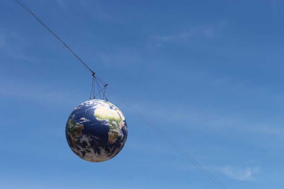 A realistic globe hanging on cables against a vivid blue sky, representing global unity.