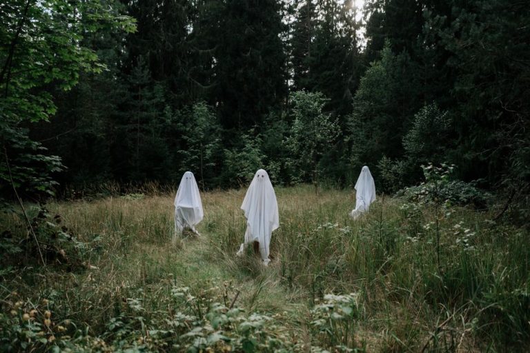 Three people dressed as ghosts in a forest setting evoke Halloween mystery and spirit.