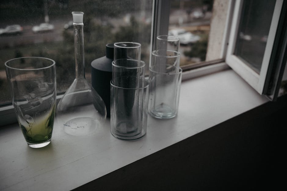 Group of glass vessels on a window sill with outdoor view.