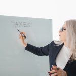Senior woman writing on whiteboard during a tax discussion in office setting.