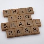 Wooden tiles form the motivational message 'This too shall pass,' highlighting resilience.
