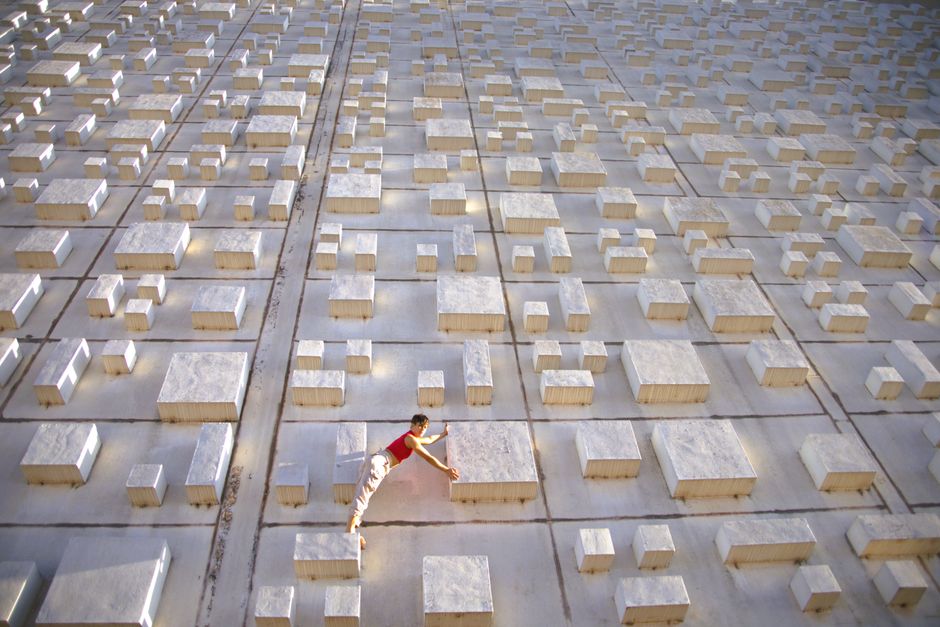 A woman artistically poses on a concrete block grid outdoors, showcasing balance and creativity.