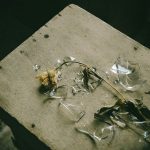 A withered flower lying on a wooden surface with broken glass nearby, creating a melancholic scene.