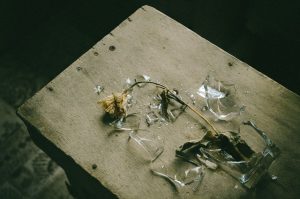 A withered flower lying on a wooden surface with broken glass nearby, creating a melancholic scene.