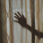 A mysterious hand silhouette casts a shadow on a textured curtain indoors, creating intrigue.
