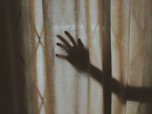 A mysterious hand silhouette casts a shadow on a textured curtain indoors, creating intrigue.