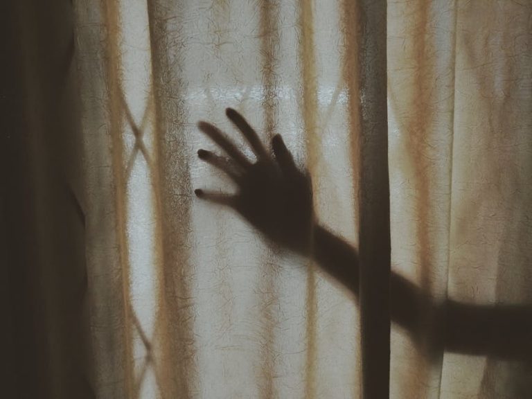 A mysterious hand silhouette casts a shadow on a textured curtain indoors, creating intrigue.
