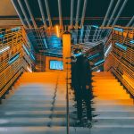 The Isolation Trap: Why Hyper-Achievement Often Leads to Strategic Blindness A person stands on a futuristic staircase surrounded by neon lights and metallic walls.