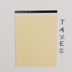 The Latency Tax: Strategy for Multi-Planetary Business Operations Close-up of a yellow legal pad and the word 'TAXES' on a white surface, ideal for finance themes.