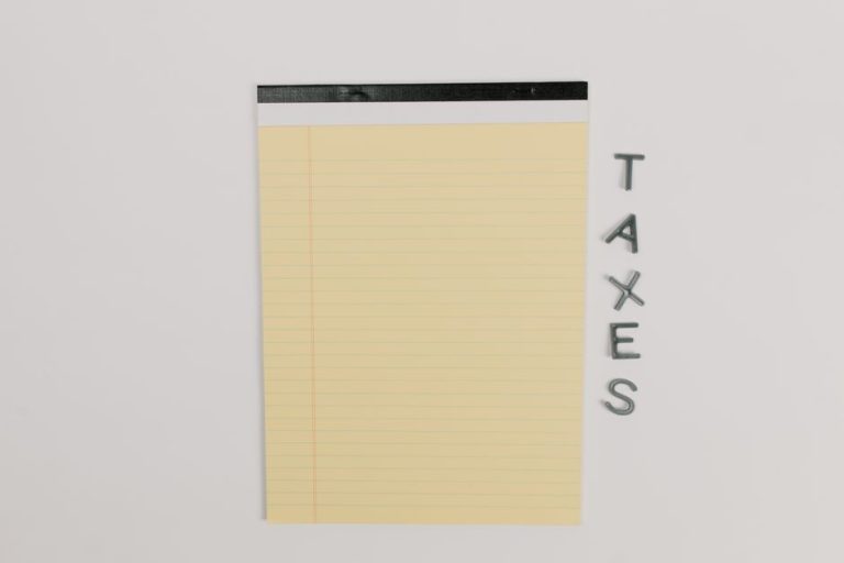 Close-up of a yellow legal pad and the word 'TAXES' on a white surface, ideal for finance themes.